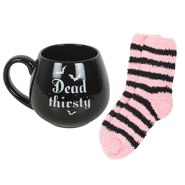 Black mug with 'Dead Thirsty' text and bat graphics, pink and black striped socks on a white background.