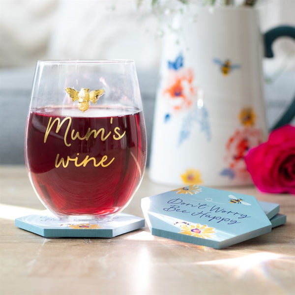 Glass of red wine with 'Mum's wine' text, butterfly decoration, on a coaster with floral design.