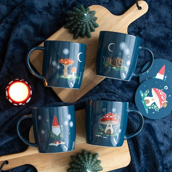 Set of blue mugs with whimsical designs on a dark surface with a candle and small trees.