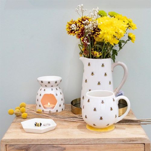 Decorative items including a pitcher, mug, and lantern on a wooden surface with flowers in the background.